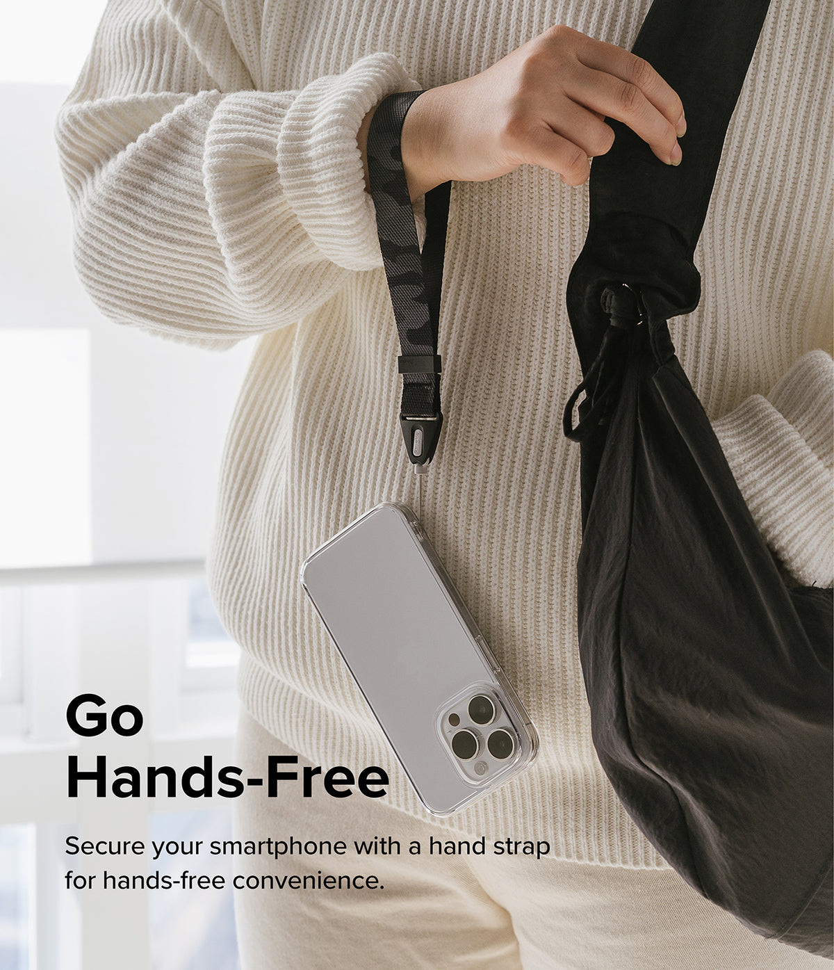 Hand Strap | Basic - A person in a white sweater wears a black camo wrist strap attached to a clear smartphone case.
