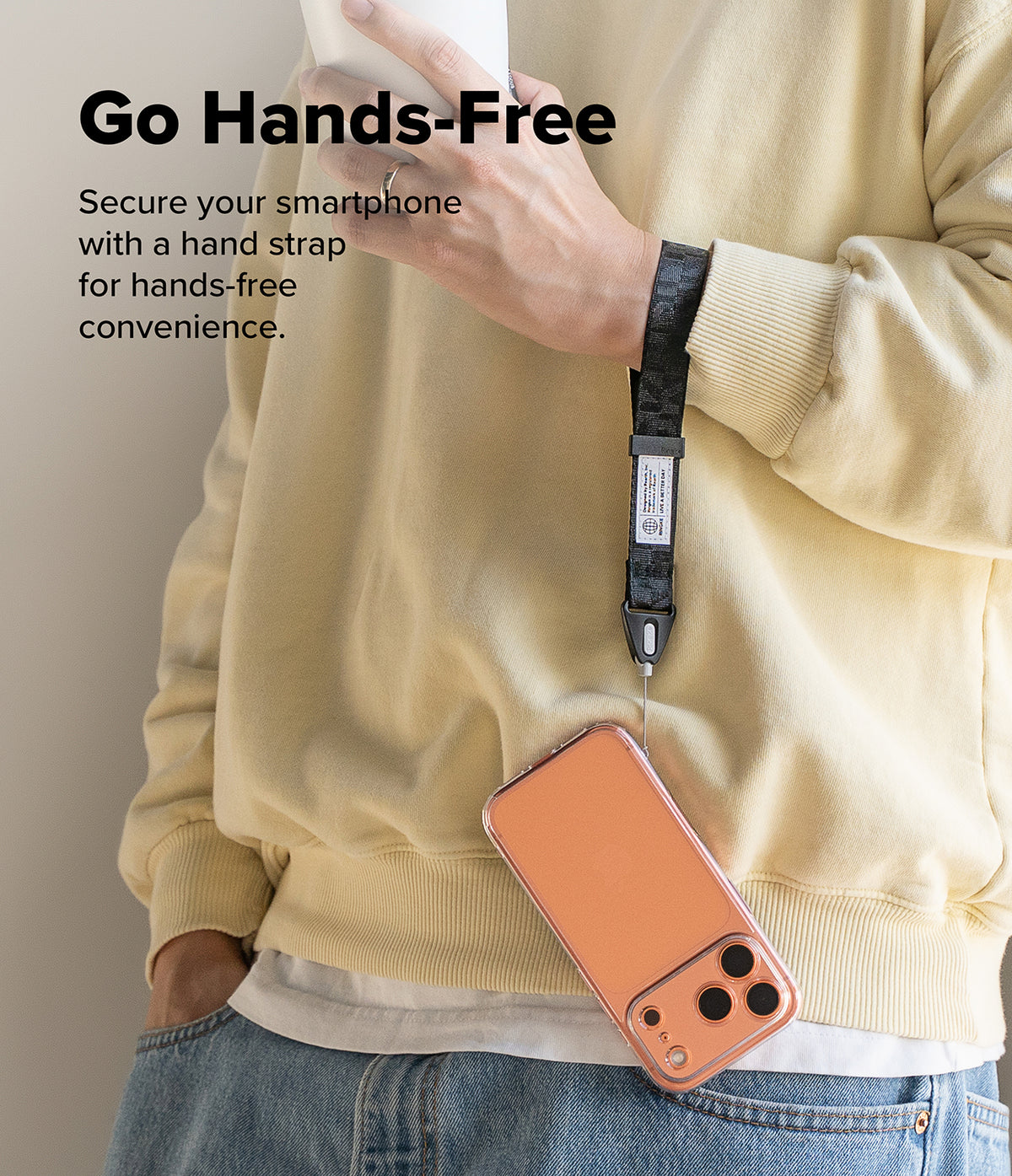 Hand Strap | Basic - A person wearing a yellow sweater holds a phone case hanging from a black patterned wrist strap.