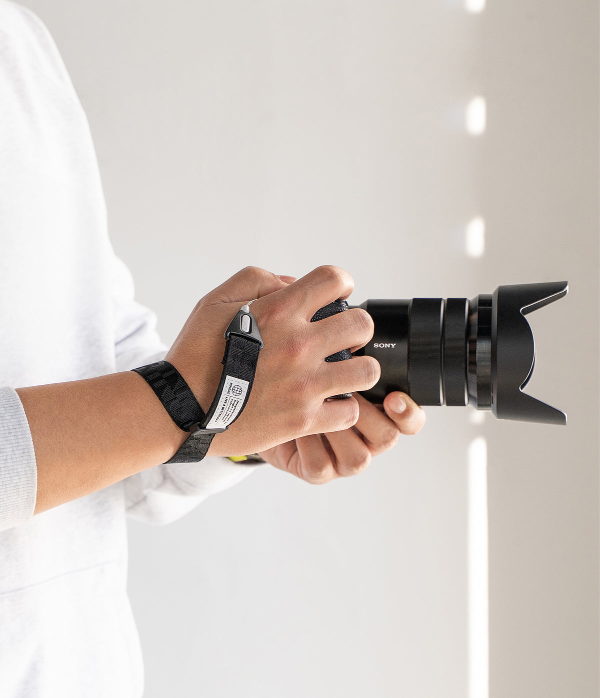 Hand Strap | Basic - A person holding a Sony camera with a black branded wrist strap secured around their forearm.