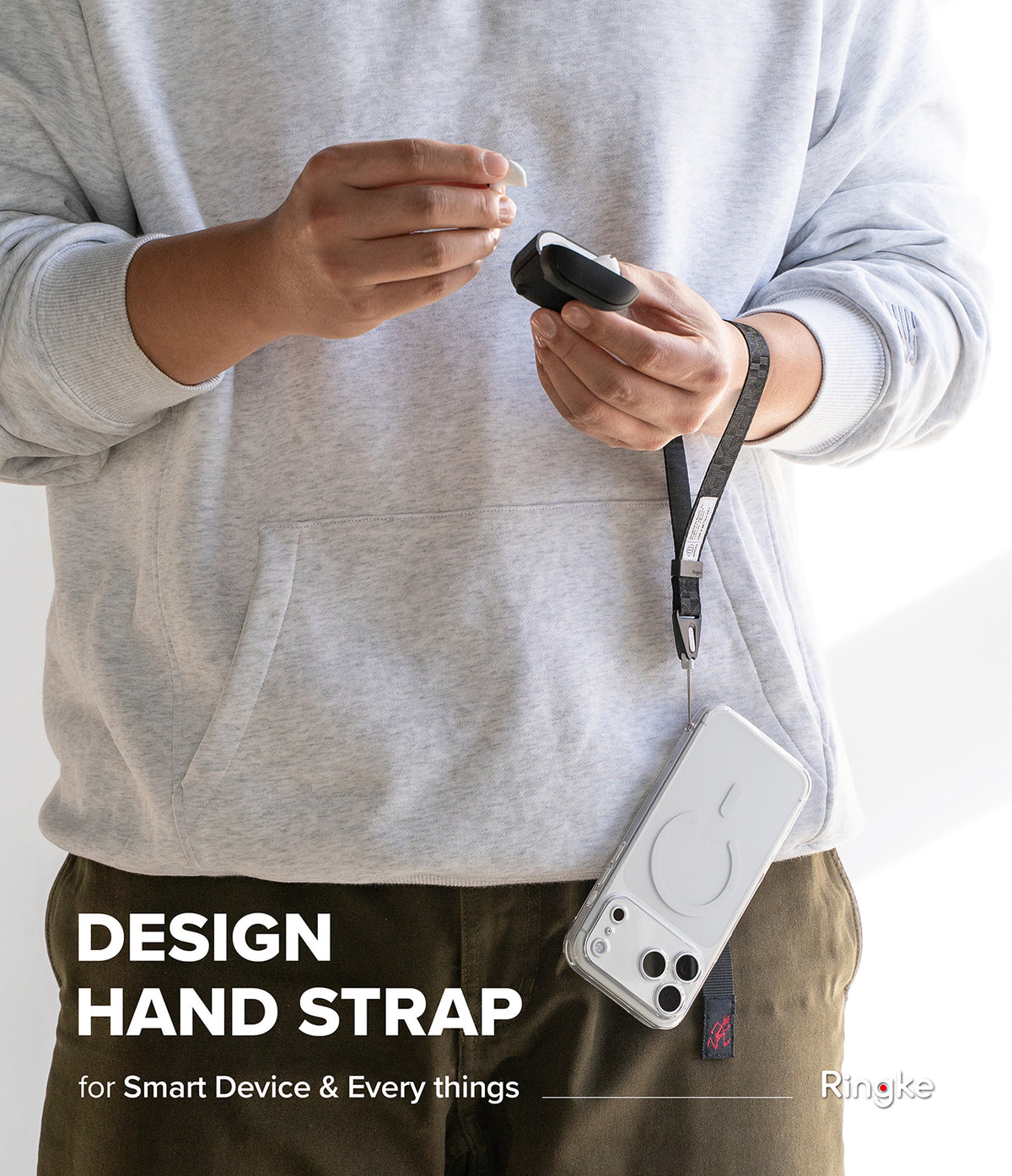 Hand Strap | Basic - Person wearing a grey hoodie holding a black earbud case attached to a phone via a black fabric hand strap.