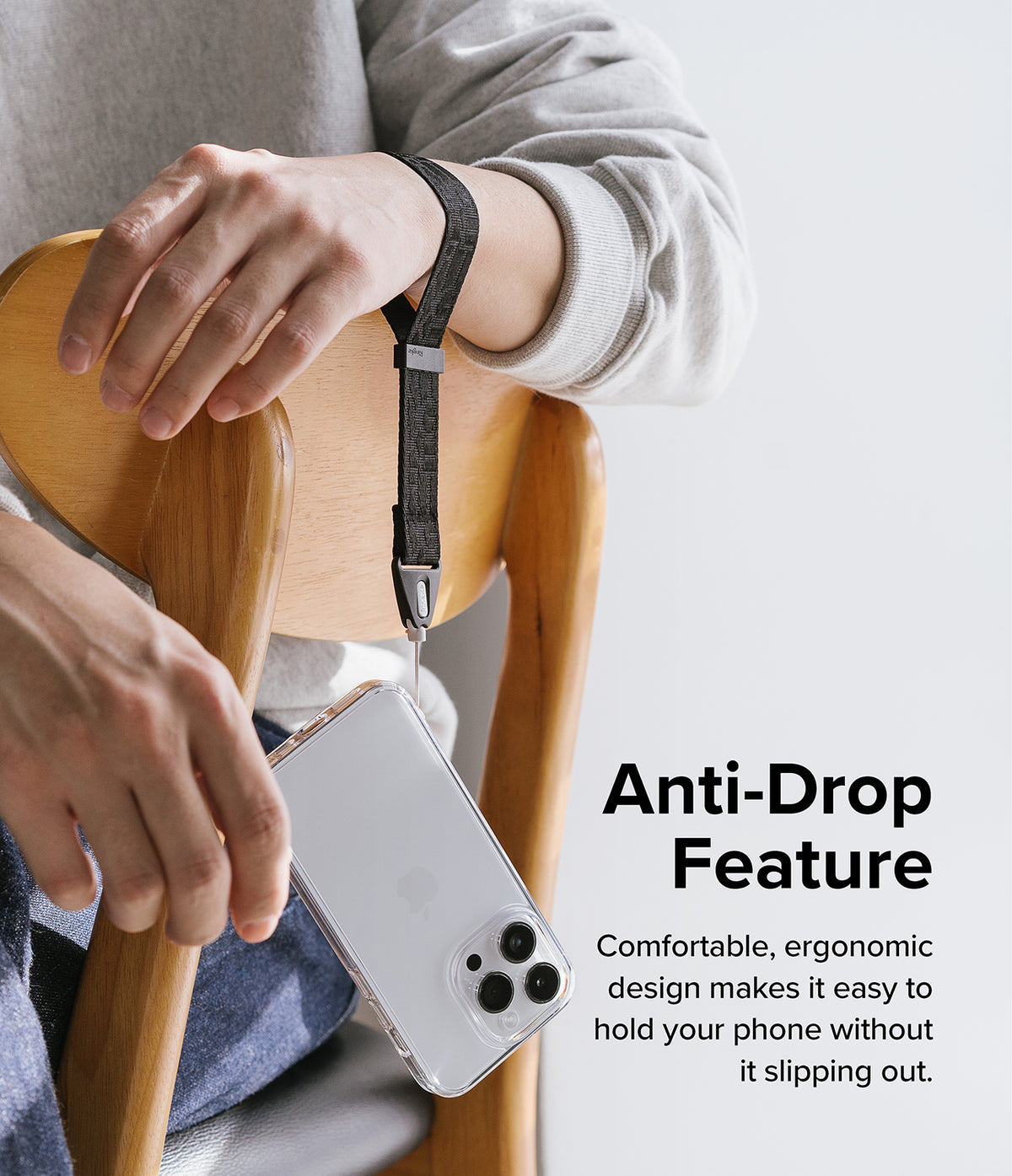 Hand Strap | Basic - A person wears a black wrist strap attached to a clear smartphone case while sitting on a wooden chair.