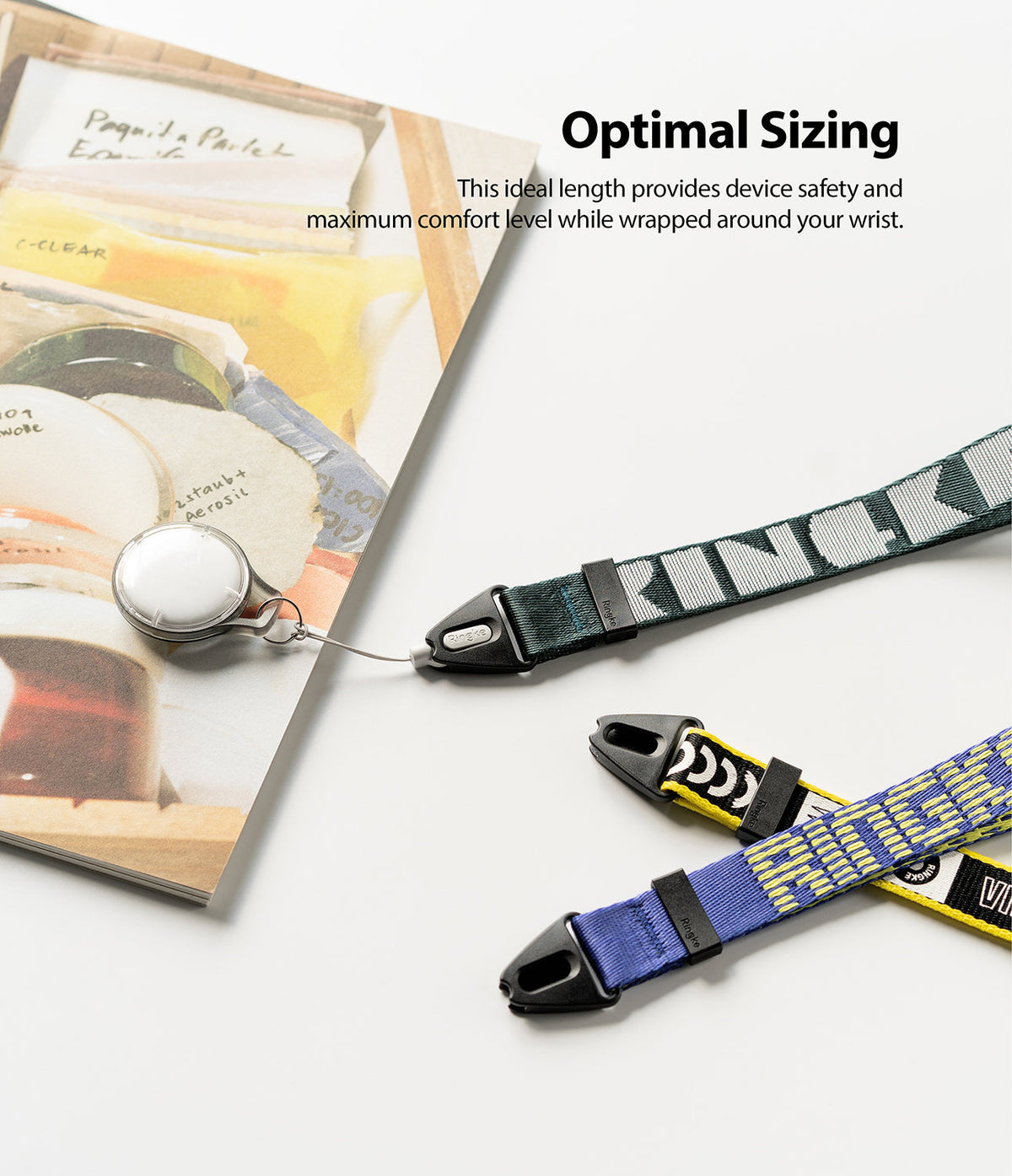 Hand Strap | Lettering - Three colorful patterned wrist straps with black clips arranged on a white surface next to a book.
