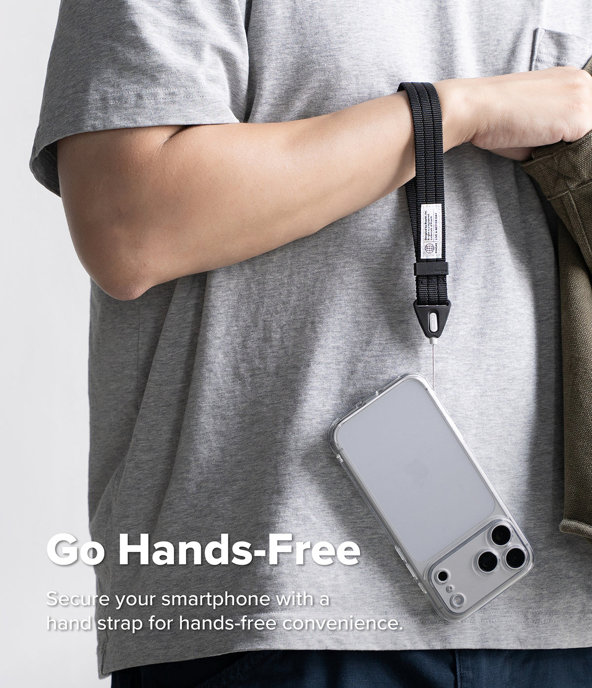 Hand Strap | Basic - A person wearing a gray T-shirt demonstrates a black phone strap with a clear case hanging from it. The text overlay reads 'Go Hands-Free' and 'Secure your smartphone with a hand strap for hands-free convenience.