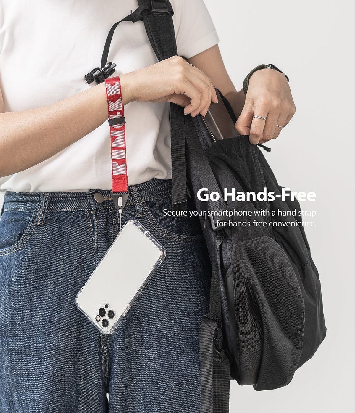 Hand Strap | Lettering - Person wearing a red Ringke branded wrist strap attached to a clear smartphone case hanging by a backpack.
