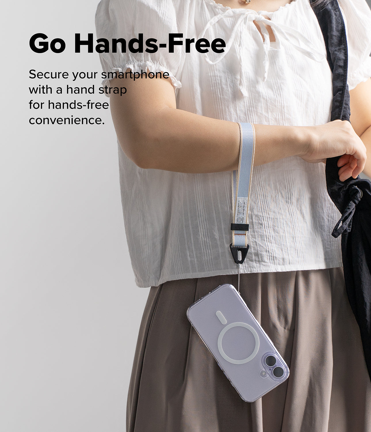 Design Hand Strap - A person wearing a light blue fabric wrist strap attached to a smartphone with a MagSafe case.
