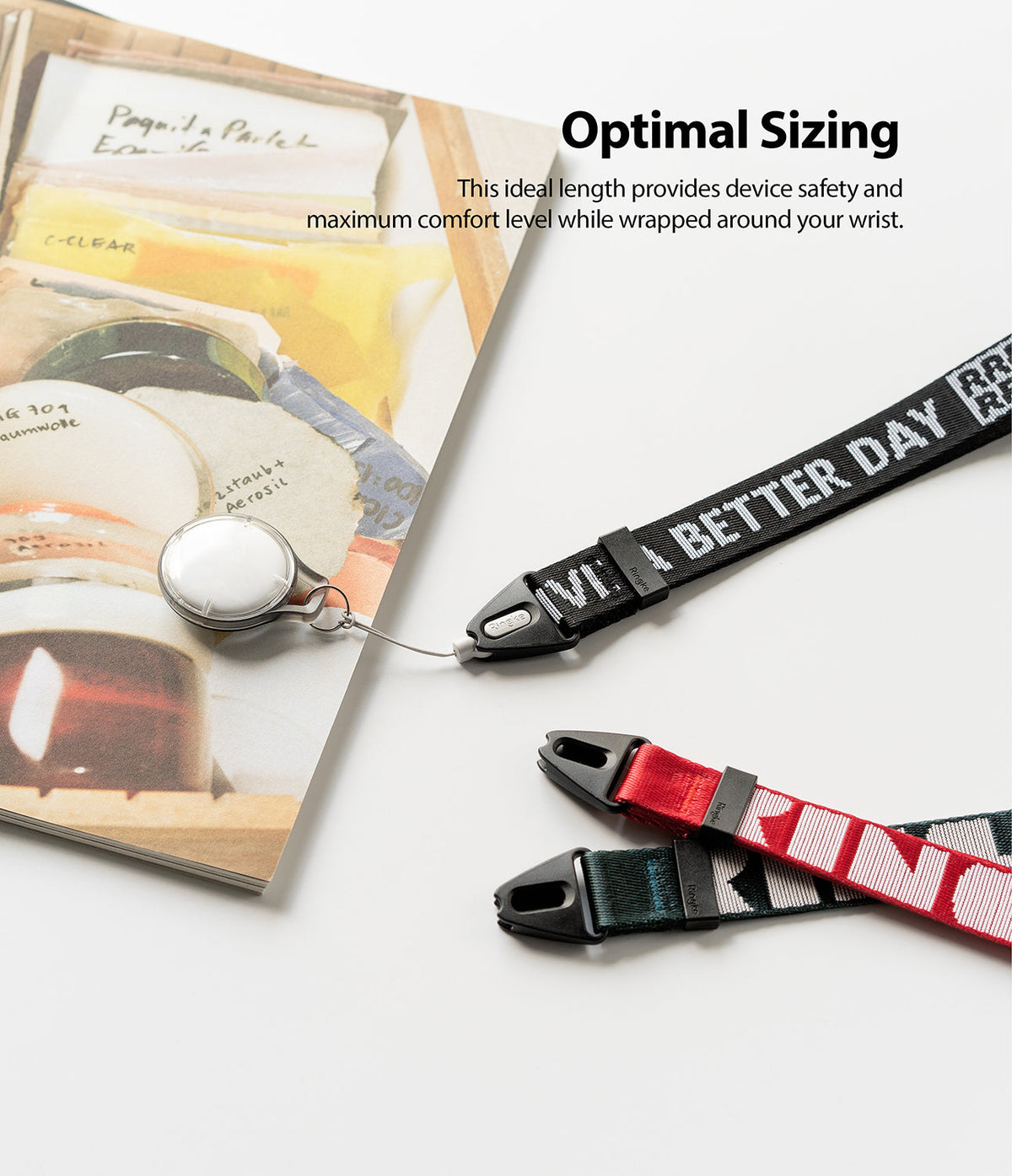 Hand Strap | Lettering - Black, red, and green wrist straps with white lettering next to a book and a small white circular tag.