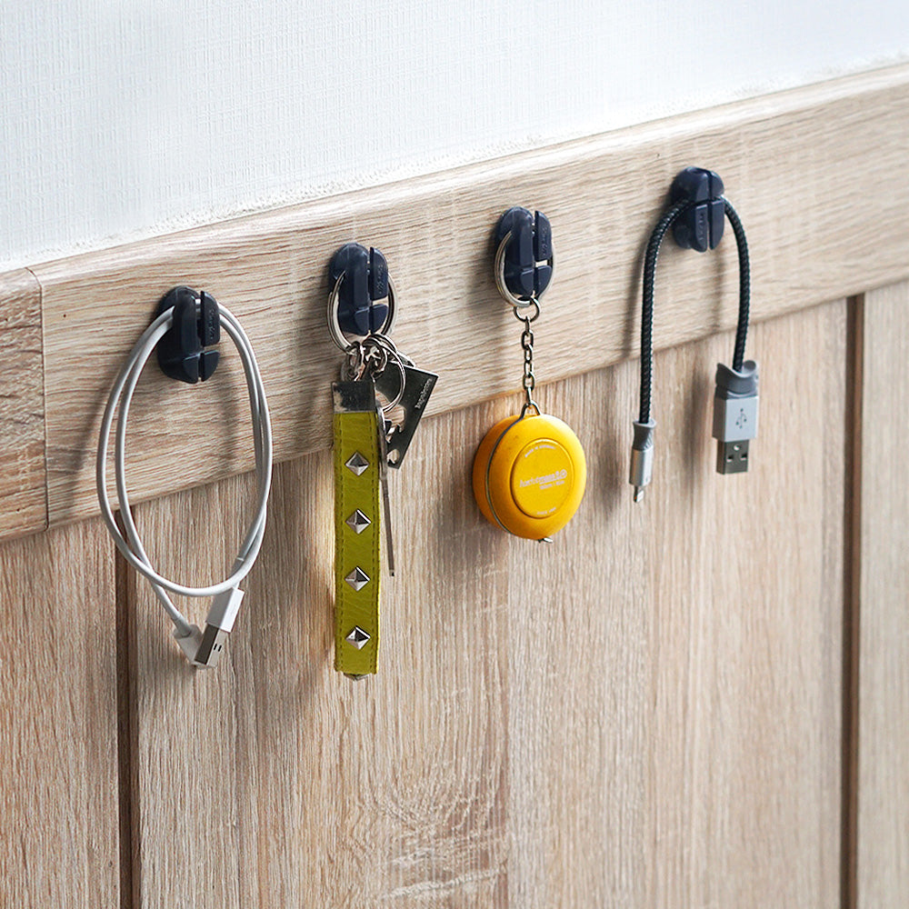 Cable Holder - Four small adhesive clips mounted on a wooden wall, holding charging cables, keys, and a measuring tape.