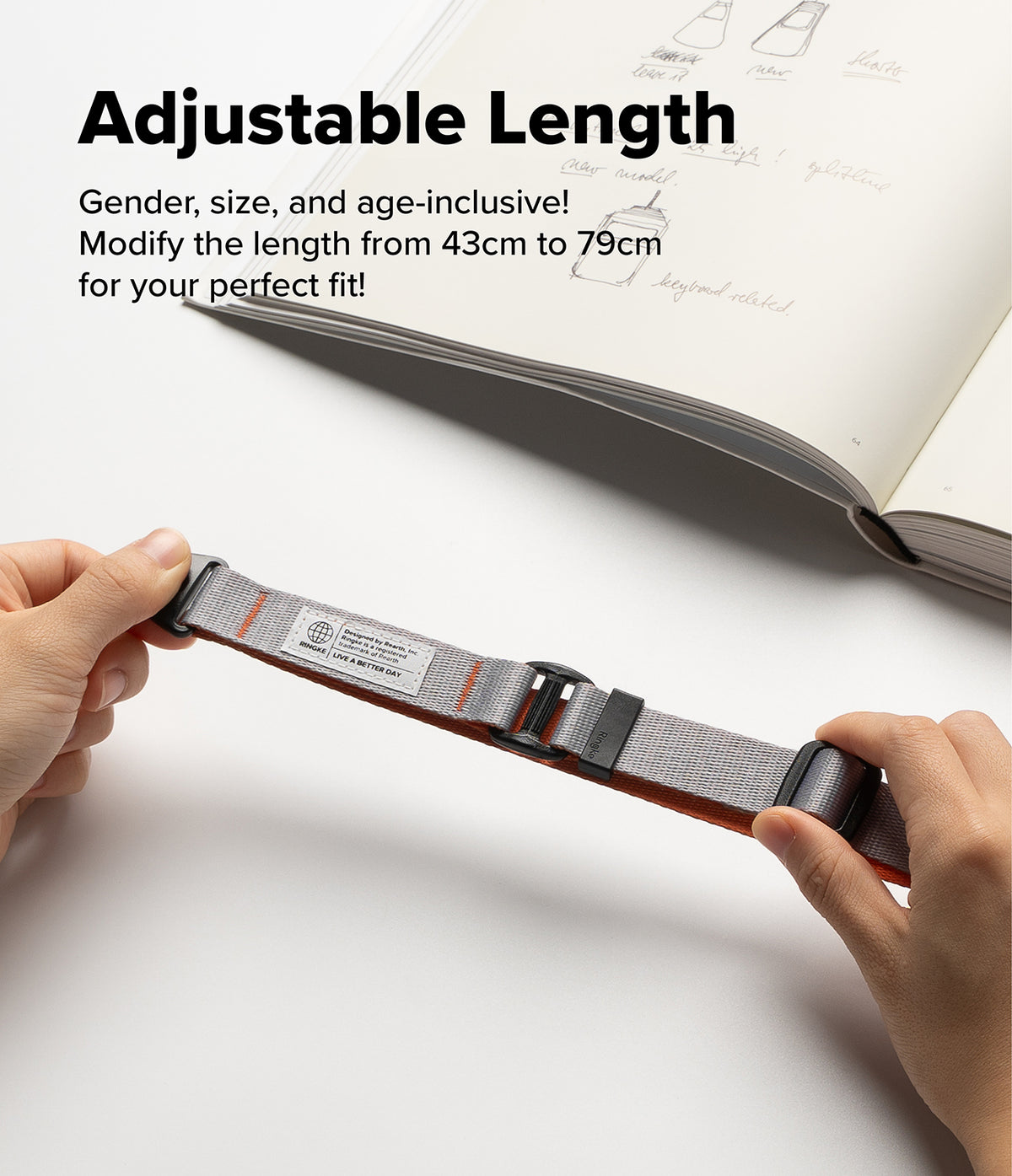 Design Lanyard Strap - Hands adjusting a grey and orange adjustable lanyard strap with black hardware over a sketchbook.