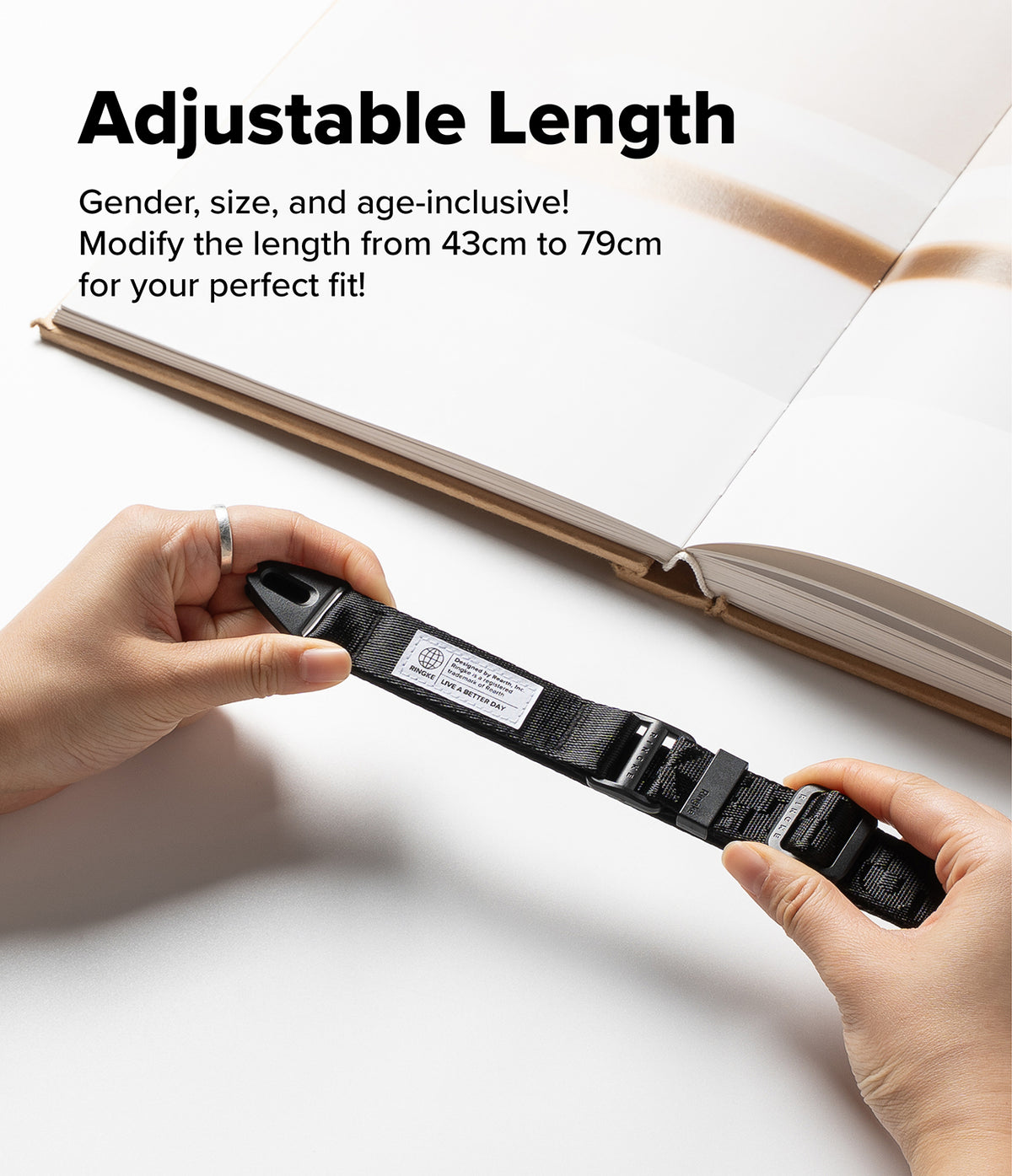 Design Lanyard Strap - Hands adjusting a black Ringke lanyard with a white brand label and adjustable buckle over a book.
