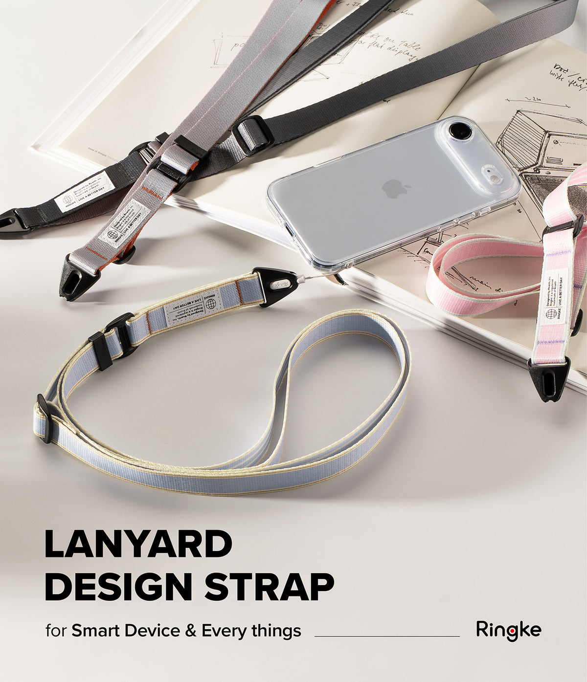 Design Lanyard Strap - Three colorful fabric lanyards with black clips arranged on a desk next to a clear phone case and notebook.
