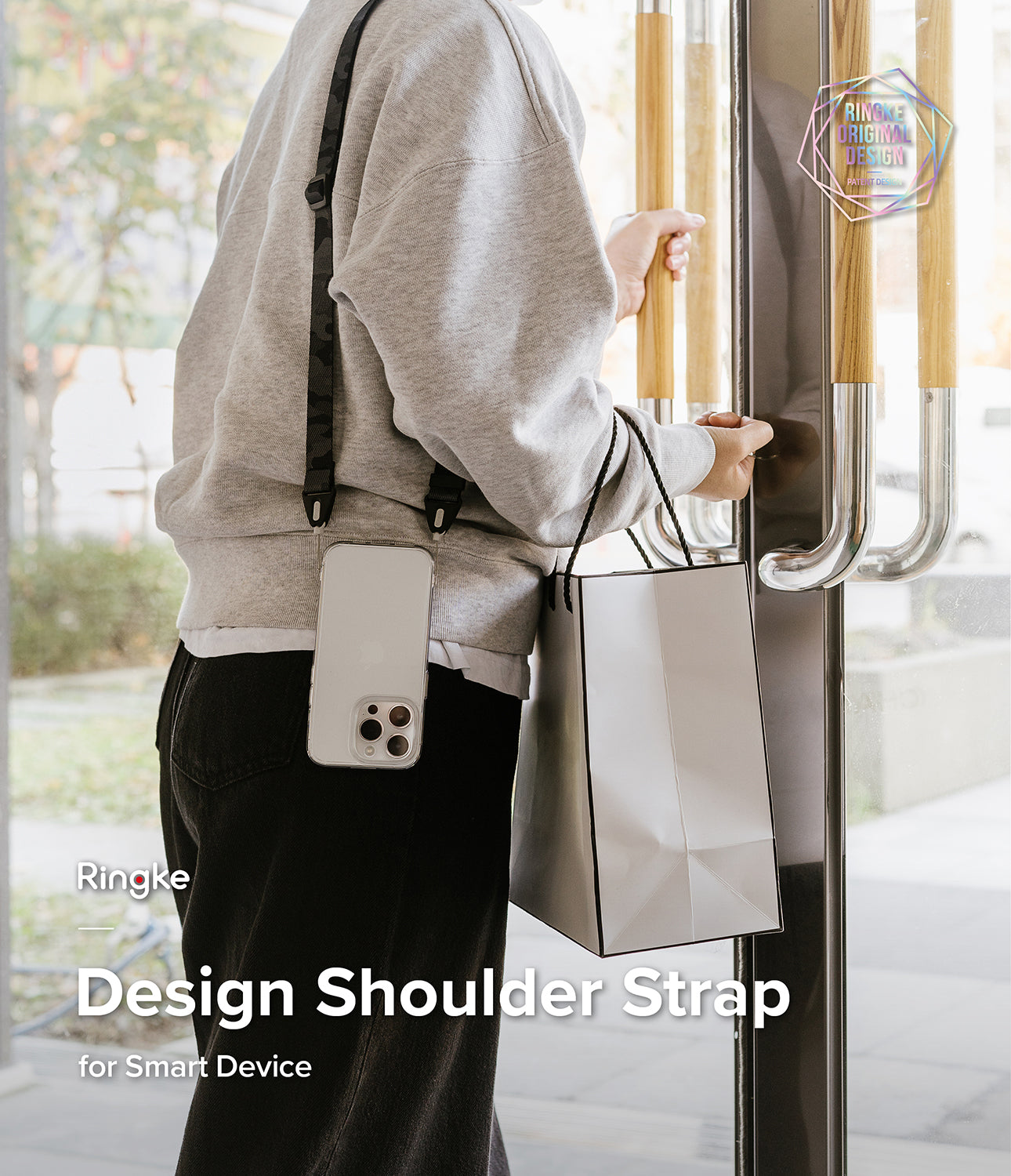 Design Shoulder Strap - Person wearing a phone on a camo shoulder strap while holding a shopping bag and opening a door.