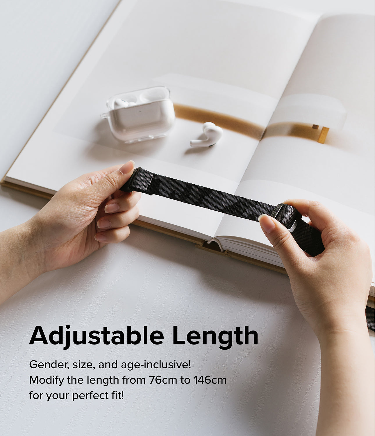 Design Shoulder Strap - Hands adjusting the length of a black camouflage patterned strap over an open book with earbuds.