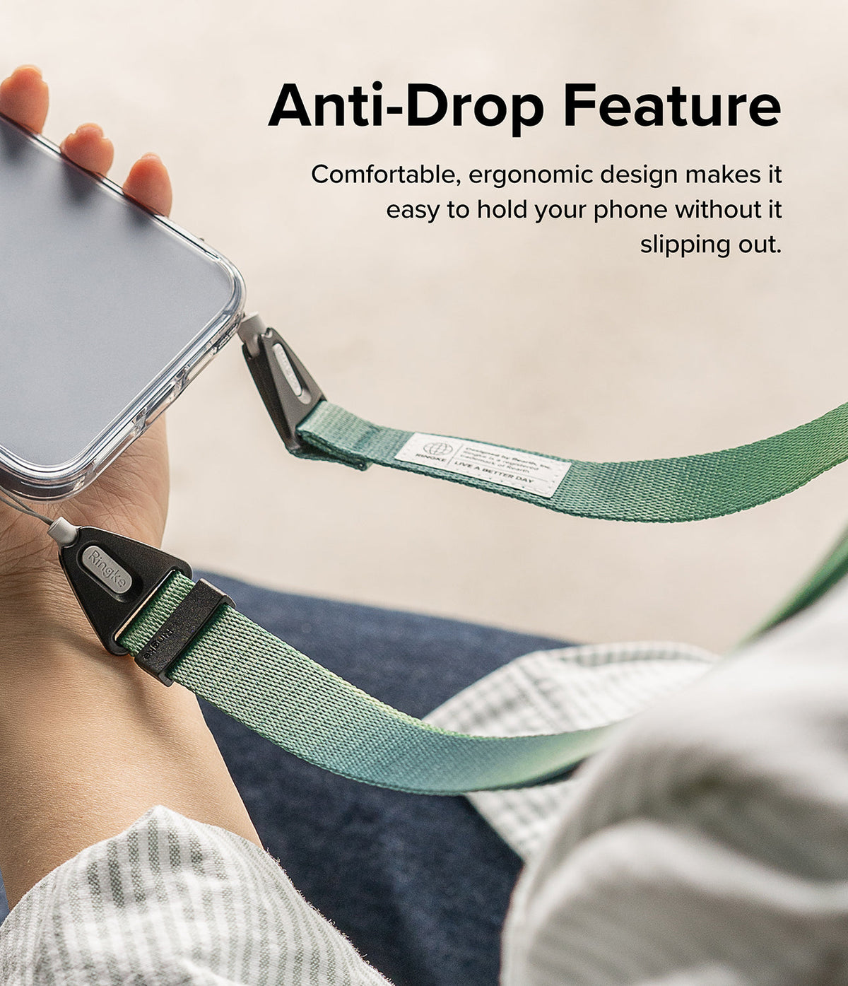 Design Shoulder Strap - A hand holding a phone secured by a green fabric strap with black clips and a branded label.