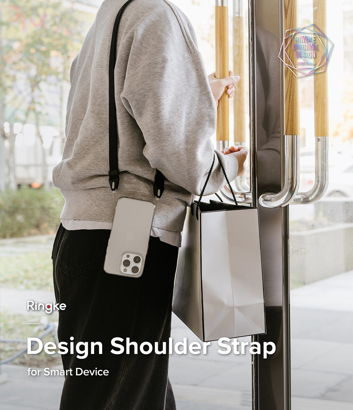 Design Shoulder Strap - A person wearing a smartphone on a black shoulder strap while holding a shopping bag at a door.