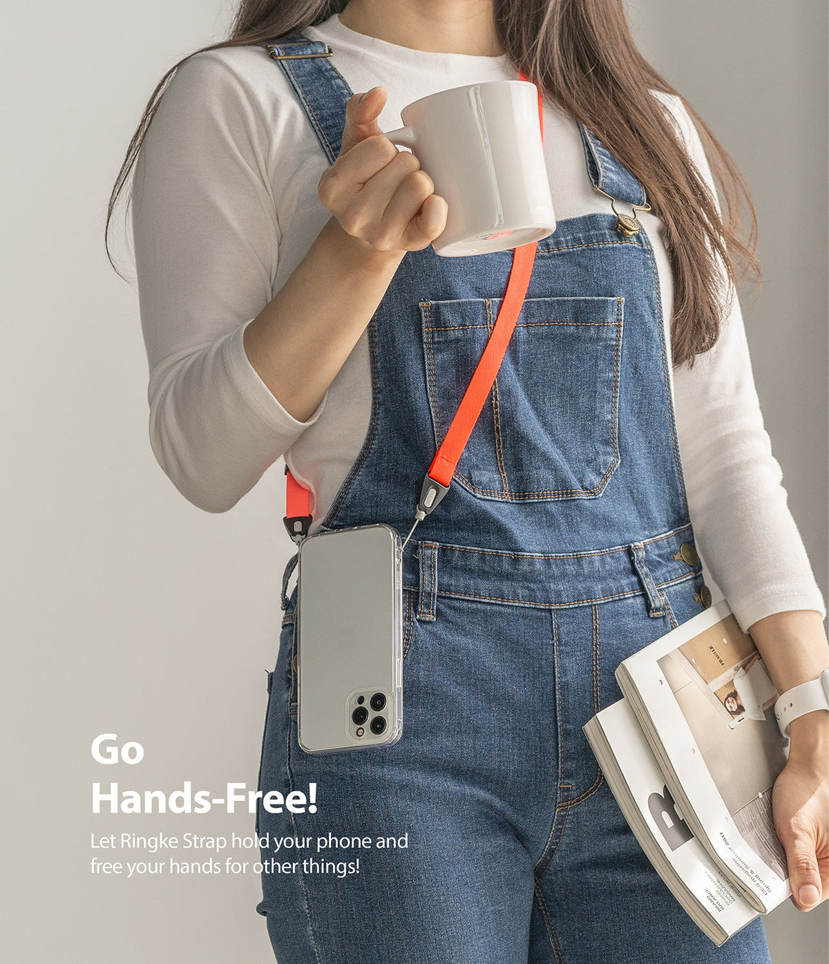 Shoulder Strap | Black / Neon Orange - Person wearing denim overalls with a neon orange phone strap holding a mug and magazines.