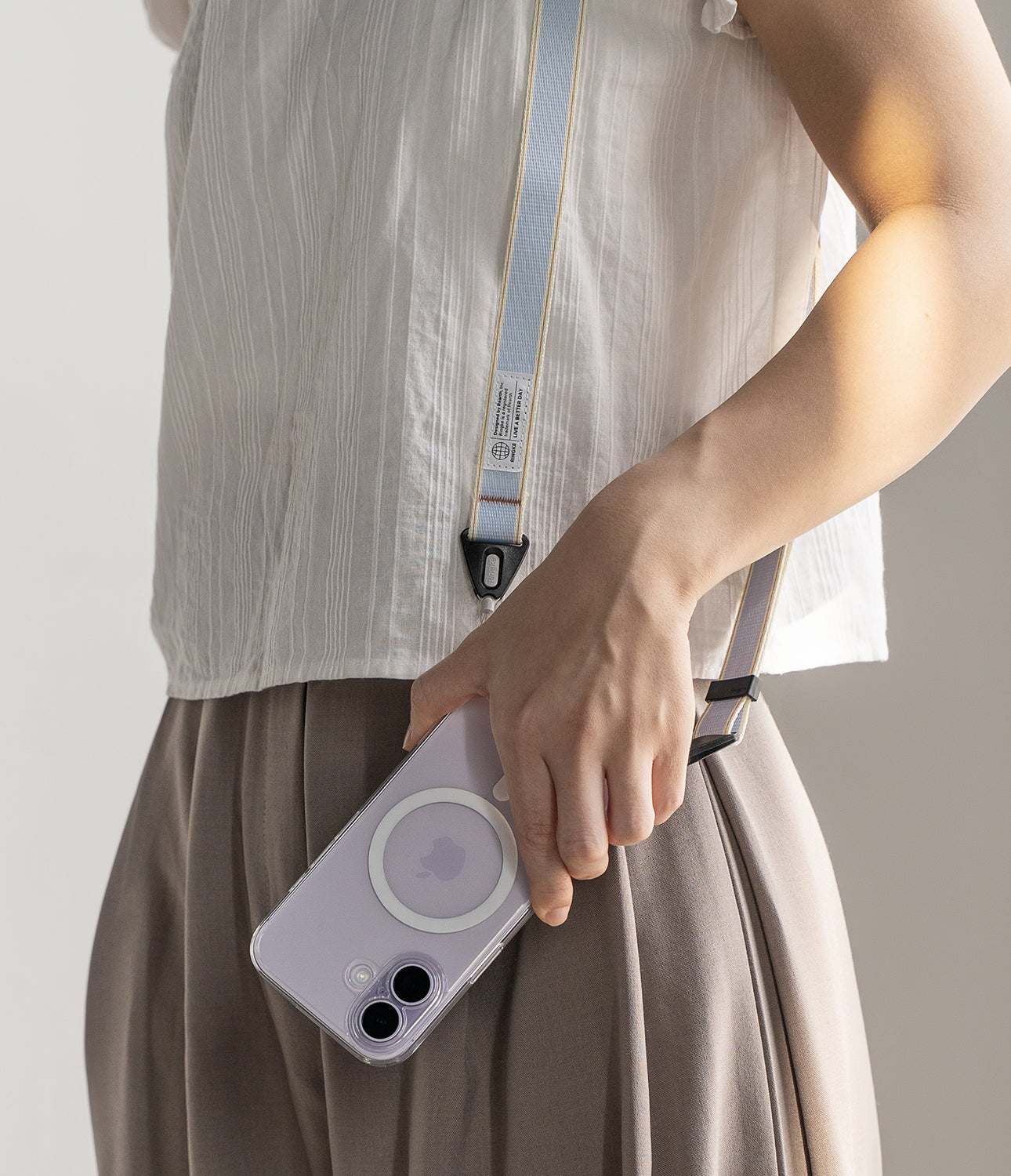 Design Shoulder Strap - A person wearing a light blue and yellow fabric phone strap attached to a clear case on a purple phone.