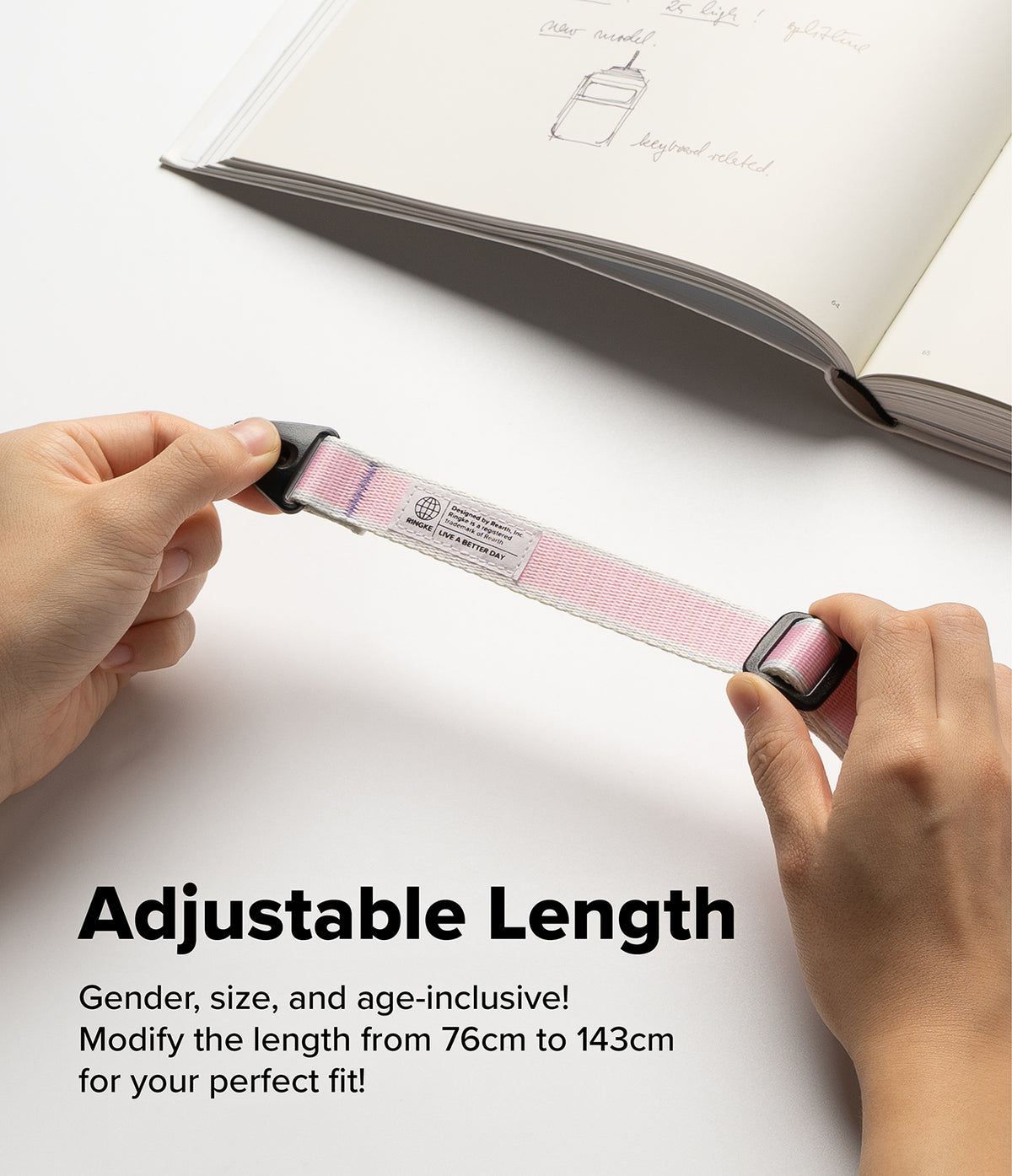 Design Shoulder Strap - Hands adjusting a pink and white fabric strap with black plastic buckles over a notebook.