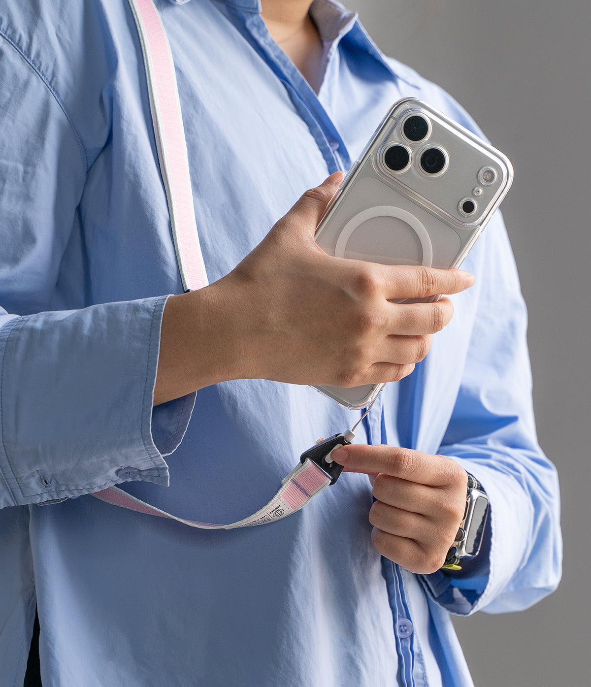 Design Shoulder Strap - A person in a blue shirt attaches a pink and white patterned phone strap to a clear smartphone case.