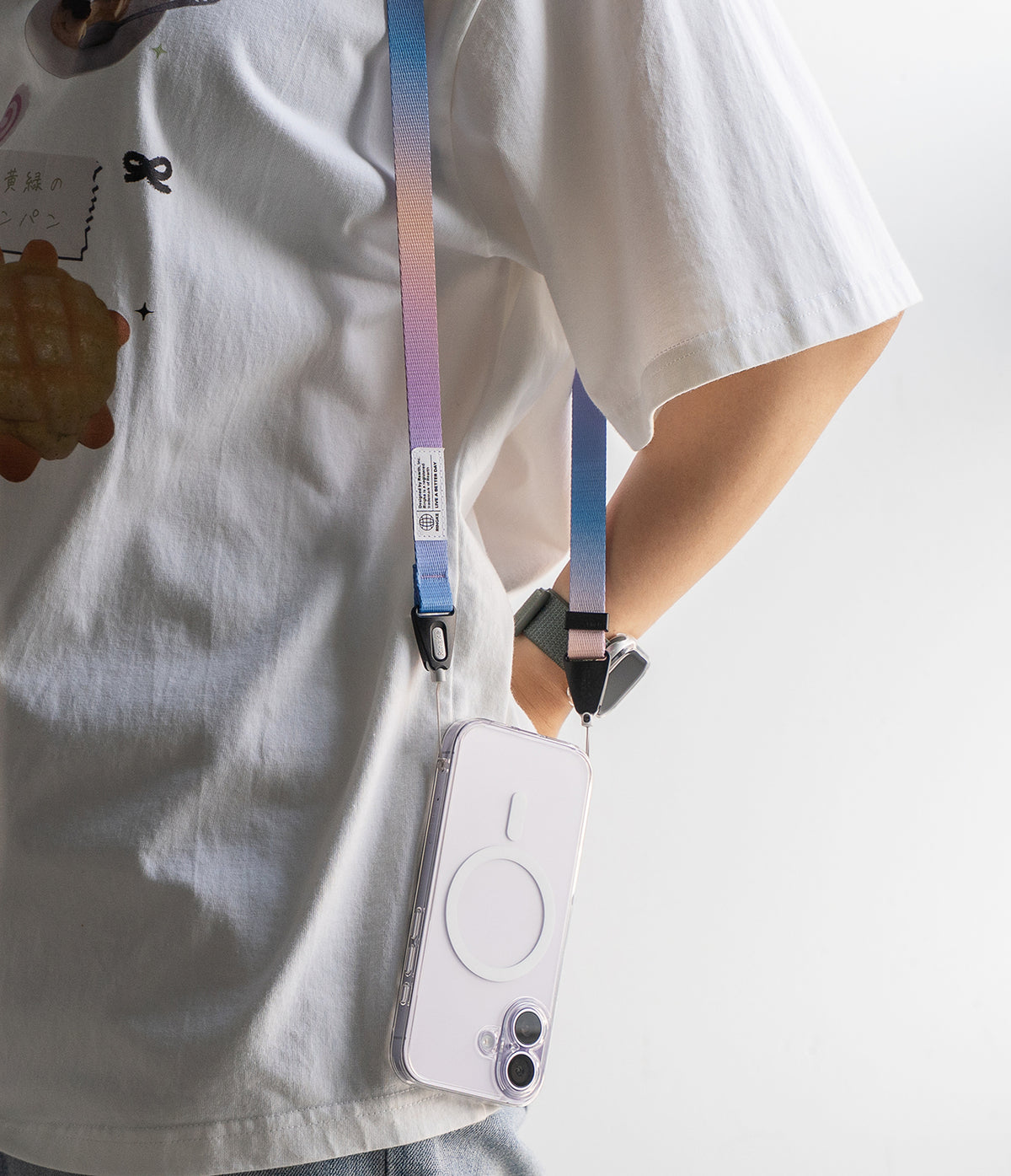 Shoulder Slim Strap - A person wearing a pastel gradient phone strap attached to a clear phone case over a white t-shirt.