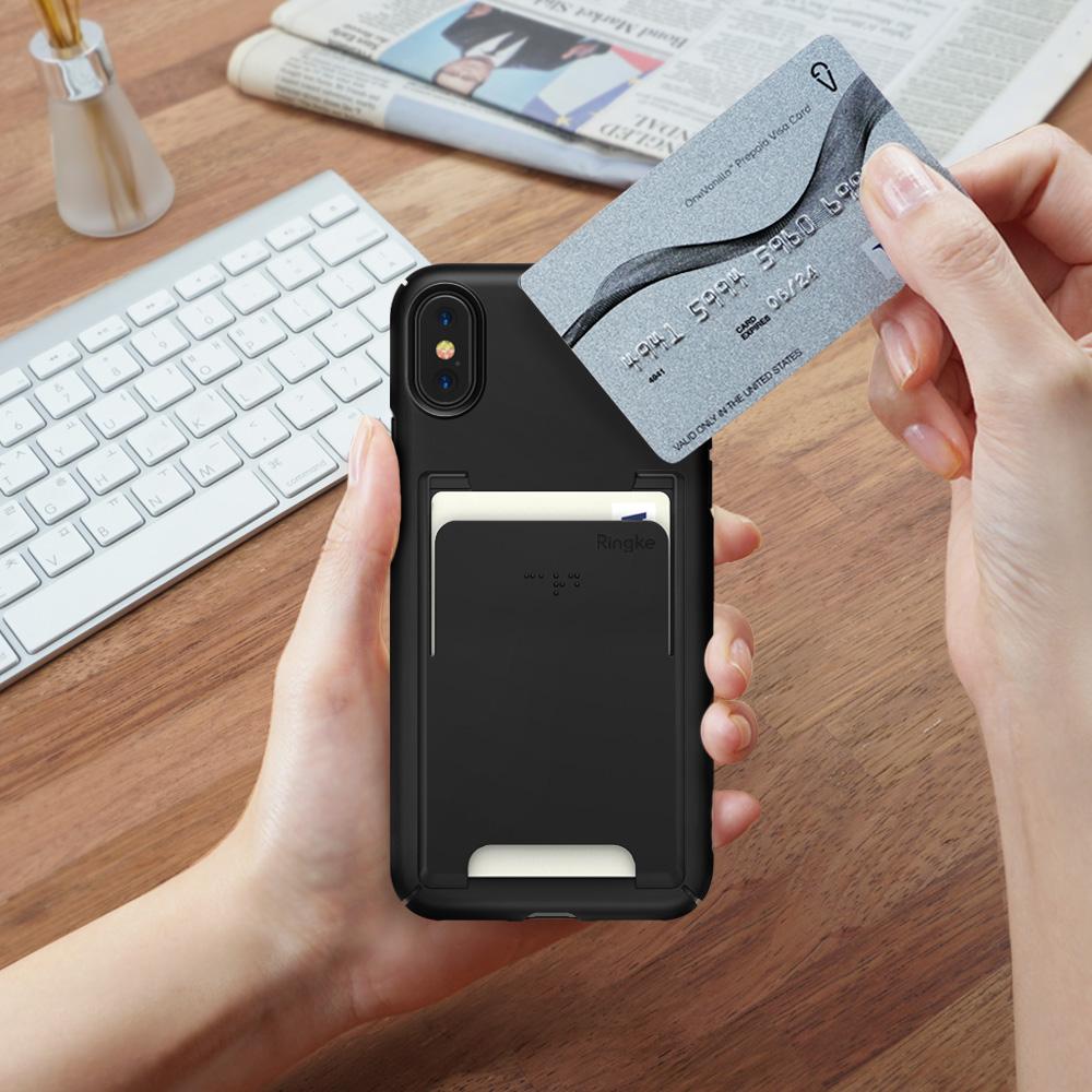 iPhone X Case | Slim + Slot Card Holder - Hands holding a black phone case with a card slot, inserting a credit card above a desk.