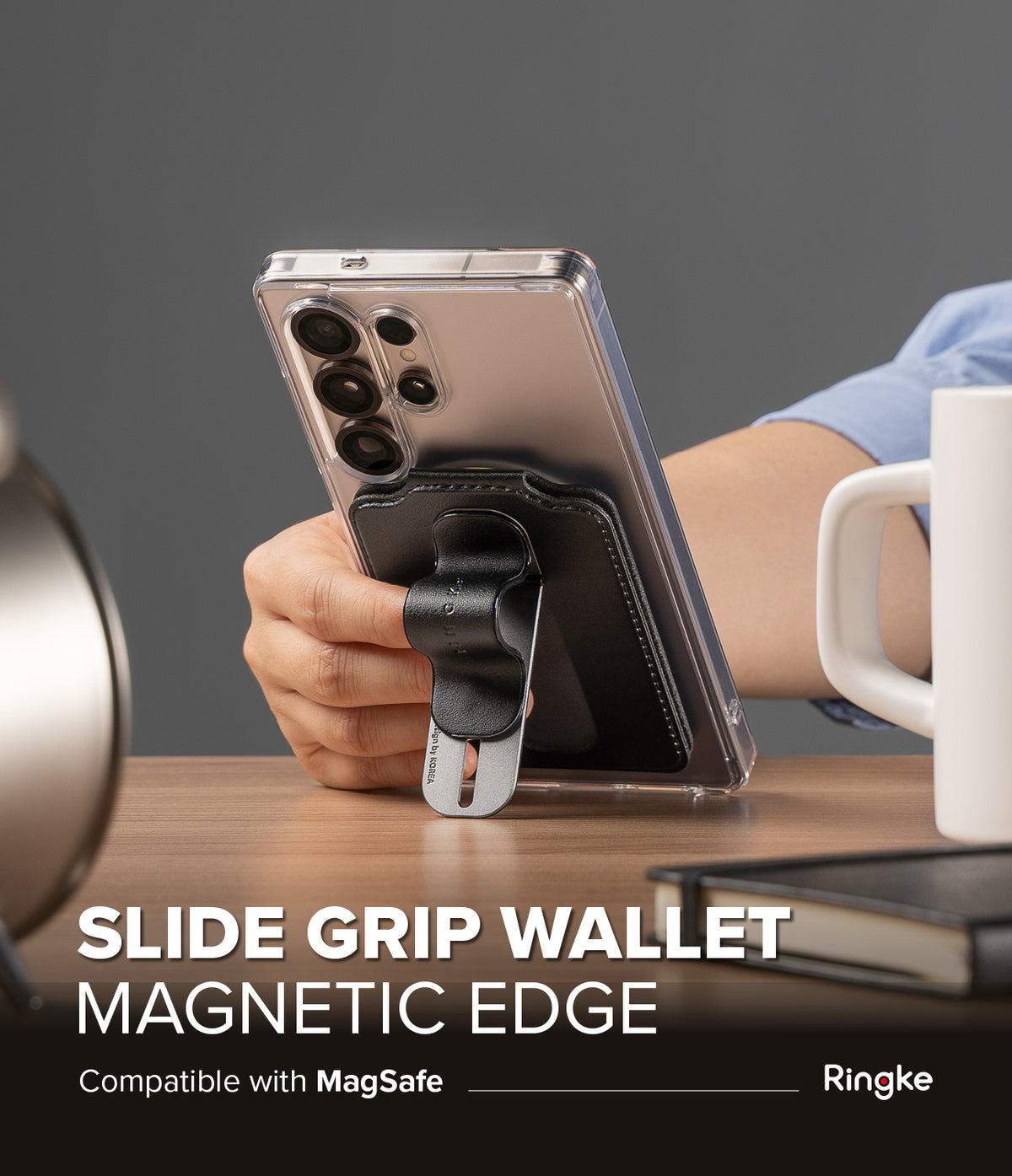 Card Holder | Slide Grip Wallet Magnetic Edge - Card Holder - Hand holding a smartphone with a black magnetic slide grip wallet attached to the back on a wooden desk.