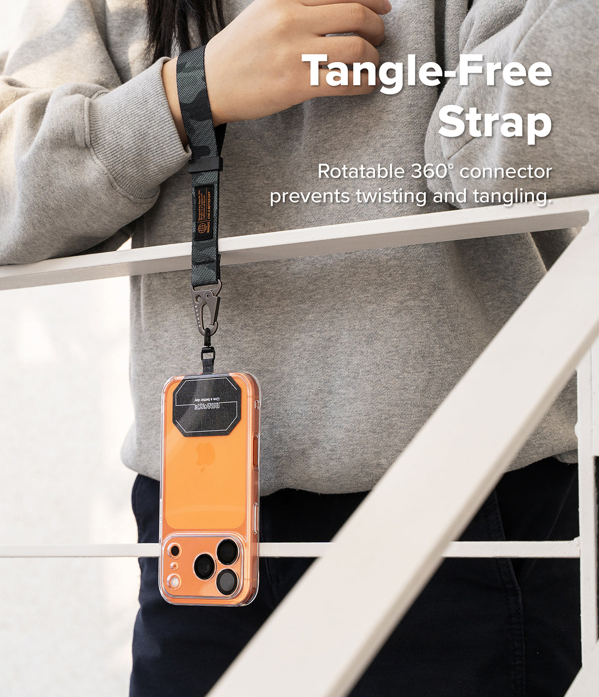 Holder Link Tactical Webbing Hand Strap - A person wearing a camo wrist strap attached to an orange phone case via a swivel.