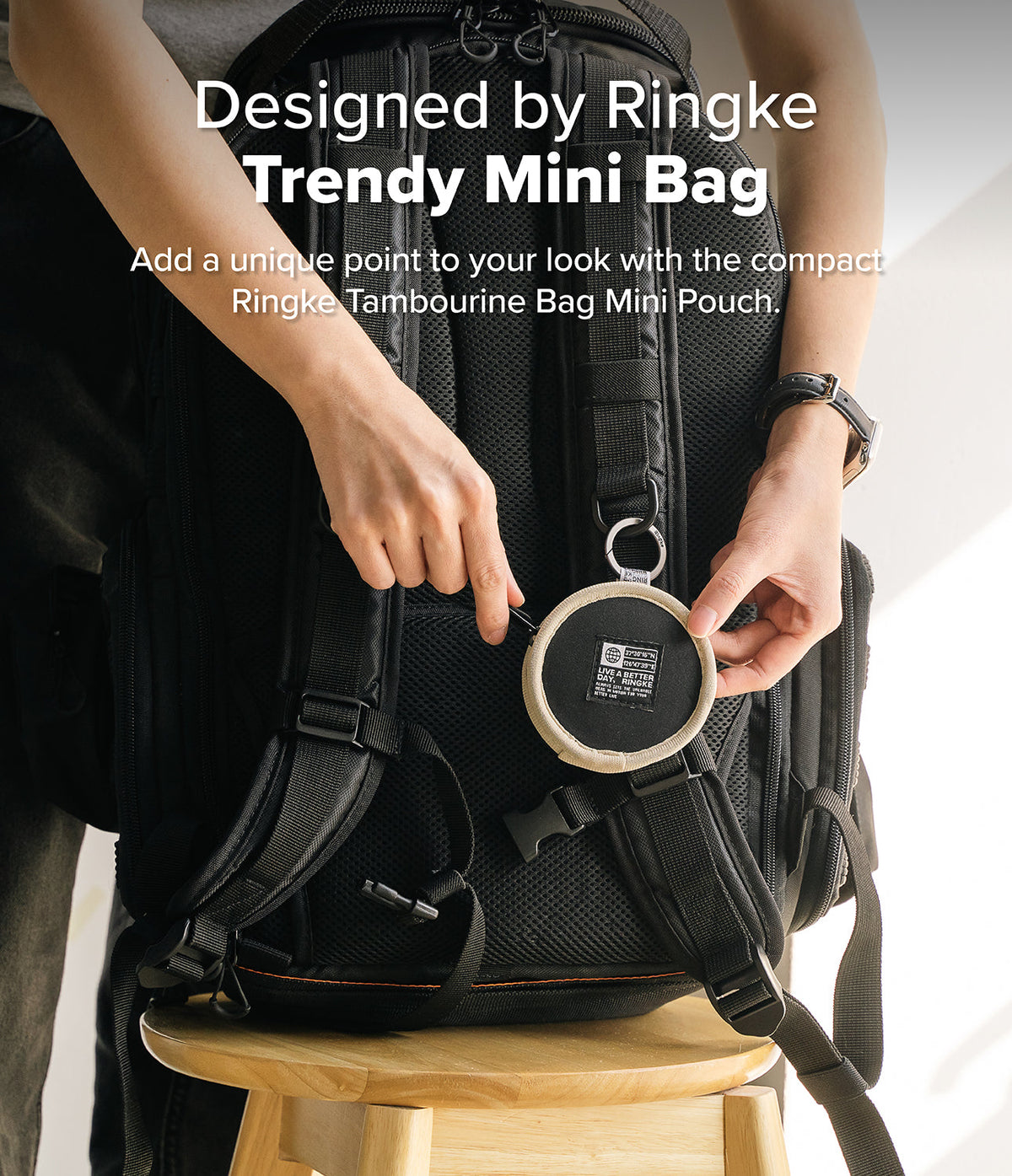 Mini Pouch | Tambourine Bag - Hands attaching a small, round, beige and black Ringke pouch to a black backpack strap.