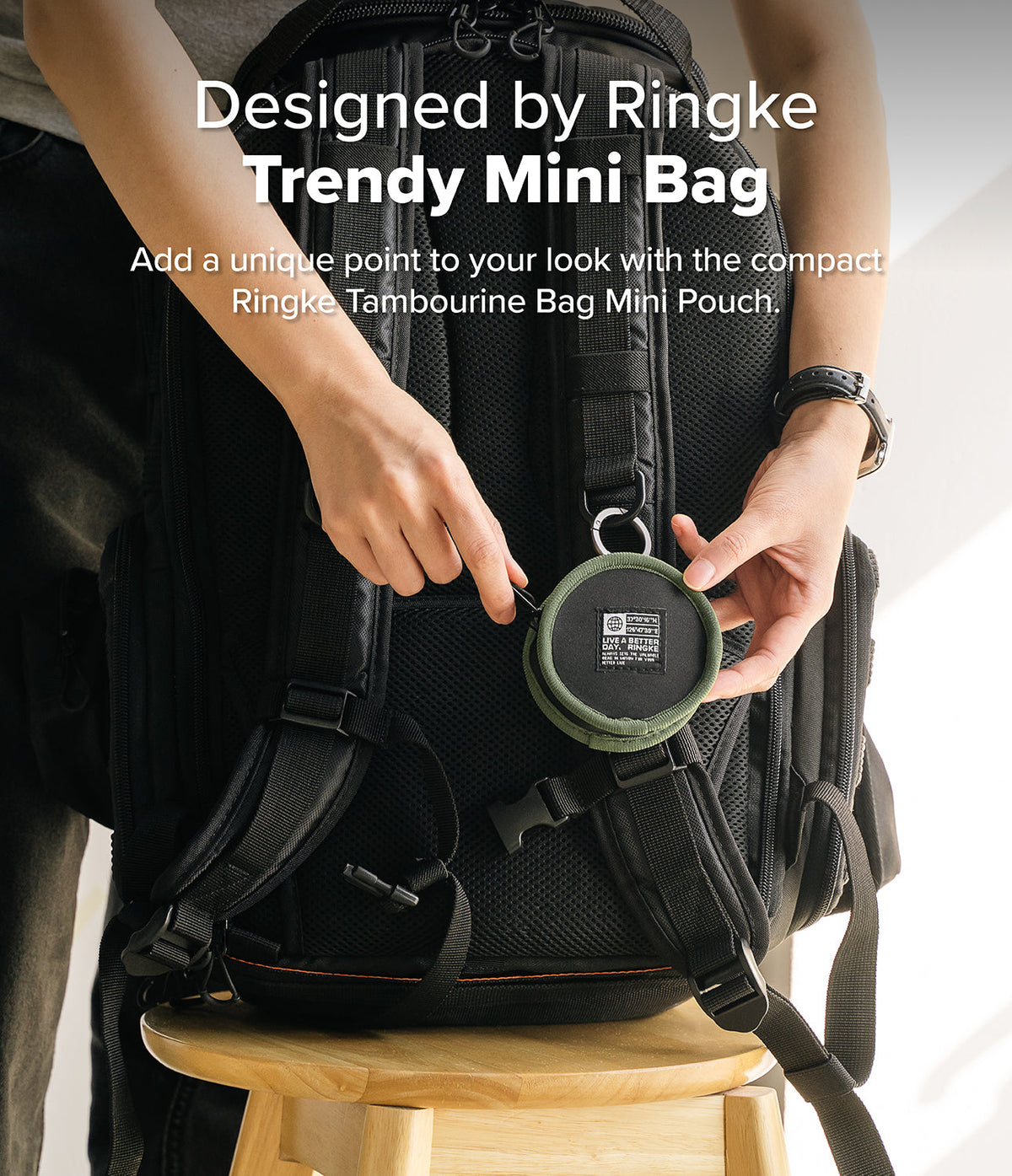 Mini Pouch | Tambourine Bag - Hands attaching a round olive green mini pouch to the strap of a black backpack.