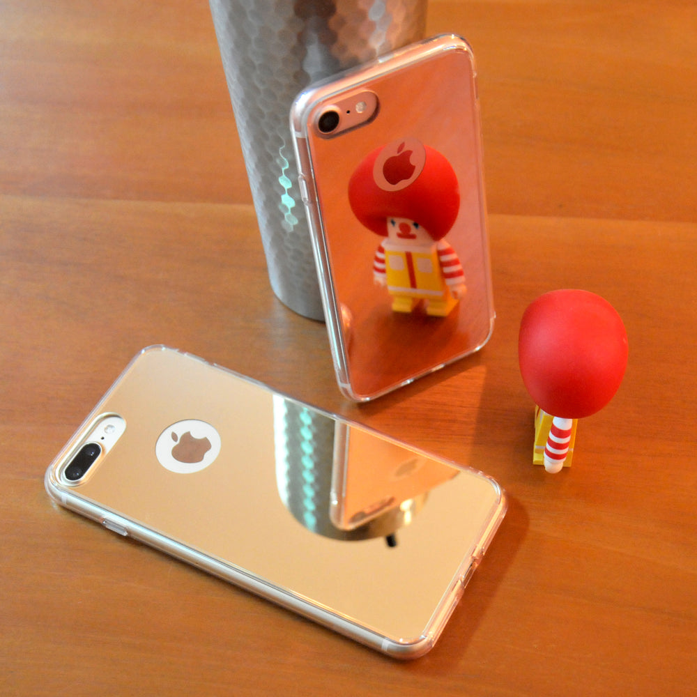 iPhone 7 Case | Mirror - Two reflective mirror-finish phone cases on a wooden table, reflecting a small Ronald McDonald figurine.