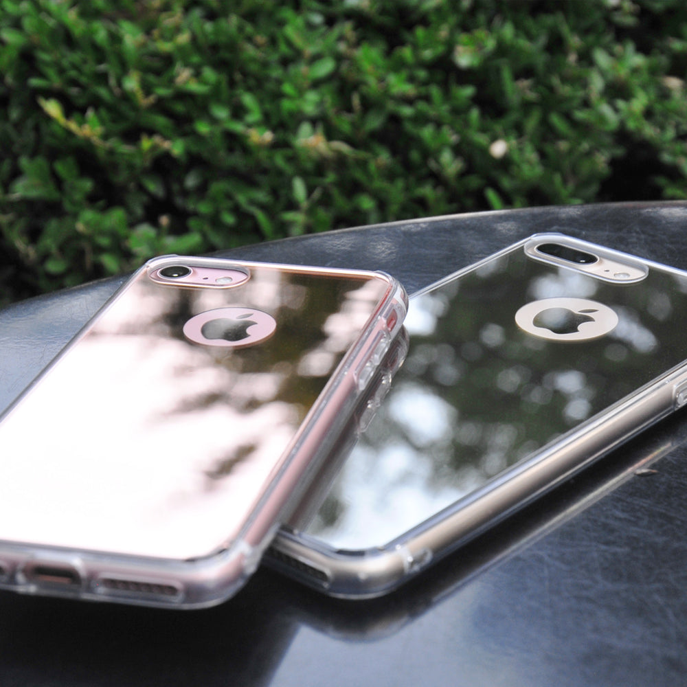 iPhone 7 Case | Mirror - Two reflective, mirror-finish iPhone cases resting on a dark surface against a green hedge.