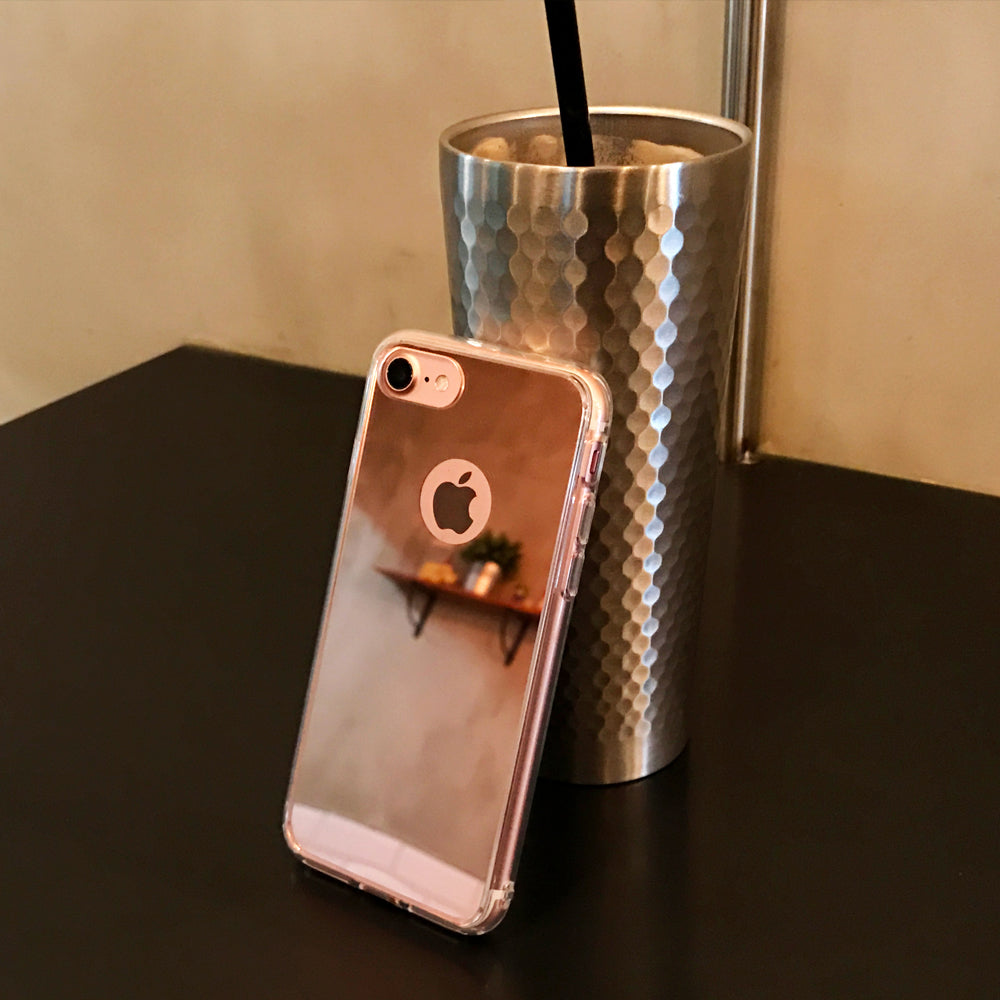 iPhone 7 Case | Mirror - A reflective rose gold iPhone case leaning against a textured metallic tumbler on a dark table.