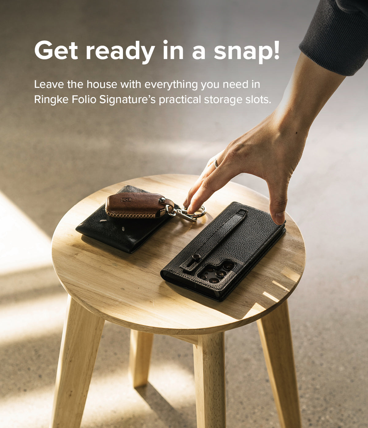 Galaxy S22 Ultra Case | Folio Signature EZ Strap - Hand reaching for a black leather phone case and wallet on a stool.
