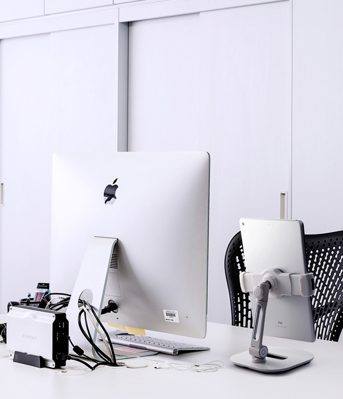Iron Tablet Stand - A silver tablet held by an adjustable stand on a white desk next to an iMac and external hard drive.