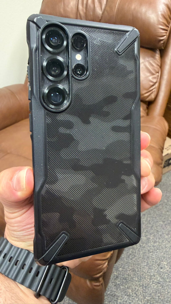 A hand holding samsung galaxy phone covered with black camo case