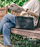 2-Way Bag - Person sitting on a wooden bench reading a magazine with a black zippered pouch resting on their lap.