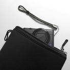 Cushion Pouch - A black camera pouch partially open to reveal a Sony compact camera with a wrist strap on a white surface.