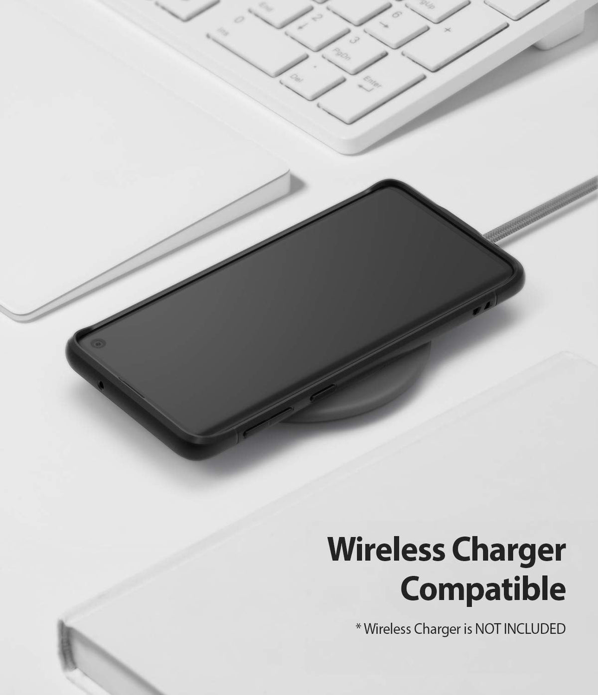 Galaxy S10 Case | Onyx - Black phone in a protective case resting on a wireless charging pad near a white keyboard.