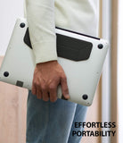 Laptop Stand - Person carrying a silver laptop with a slim, black adhesive stand attached to the bottom.