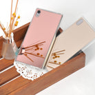 Xperia Z5 Premium Case | Mirror - Rose Gold - Two reflective rose gold phone cases resting in a wooden tray with a reed diffuser.