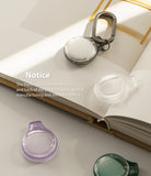 AirTag Case | Slim [1 Pack] - Clear and colored AirTag cases on a book with a notice about manufacturing parting lines.