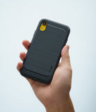 iPhone XR Case | Onyx - Hand holding a black brushed-metal texture phone case with a yellow camera cutout against white.