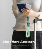 Cam Buckle Hand Strap - Person holding a phone with a green lanyard attached, standing next to a suitcase.