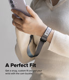 Cam Buckle Hand Strap - Hand holding a phone with a wrist strap, wearing a beige sweater on a light background.