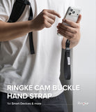 Cam Buckle Hand Strap - A person wearing a white t-shirt holds a silver smartphone with a black Ringke camera buckle hand strap attached. The person is pointing at the strap.