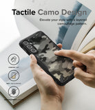 Galaxy A34 Case | Fusion-X - Hands holding a phone with a black camouflage case, featuring icons for grip, anti-discoloration, and anti-fingerprint.