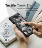 Galaxy A54 Case | Fusion-X - Hands holding a black phone case with a tactile, layered camouflage pattern and feature icons.