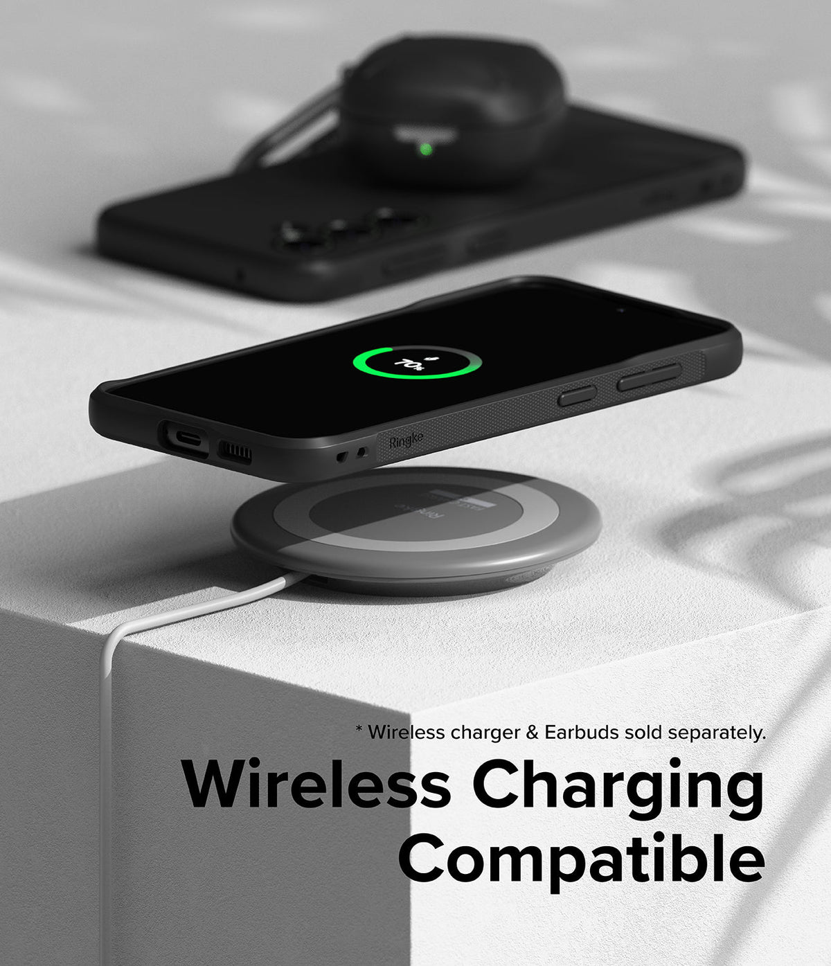 Galaxy S23 FE Case | Onyx - A black phone in an Onyx case wirelessly charging on a pad with earbuds in the background.
