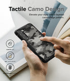 Galaxy S23 Case | Fusion-X - Hands holding a black phone case with a textured, layered camouflage pattern and protective icons.