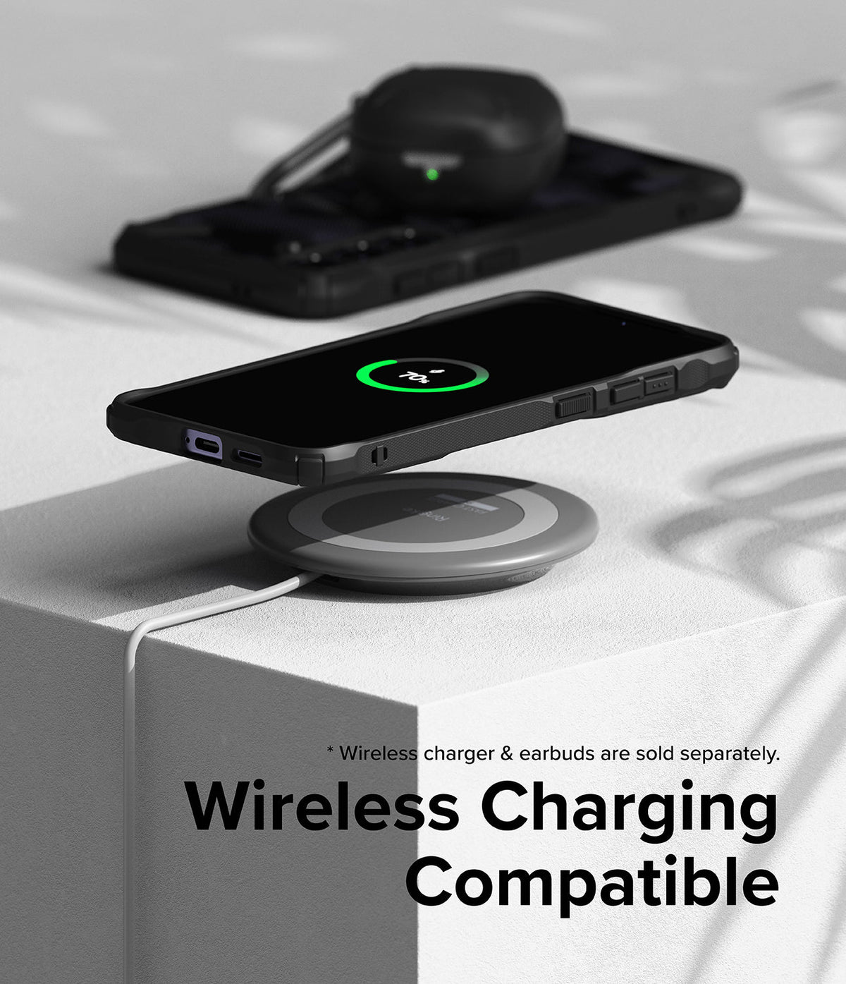 Galaxy S24 Plus Case | Fusion-X - Galaxy S24 Plus in a black case wirelessly charging on a pad with earbuds in the background.
