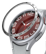 Galaxy Watch 6 Classic 47mm | Bezel Styling - Galaxy Watch 6 Classic 47mm | A metallic bezel ring hovering above a silver smartwatch with a red analog watch face.